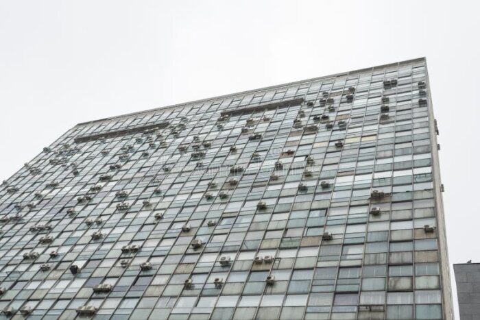 Modern byggnad med glasfasad och många luftkonditioneringar mot en grå himmel.