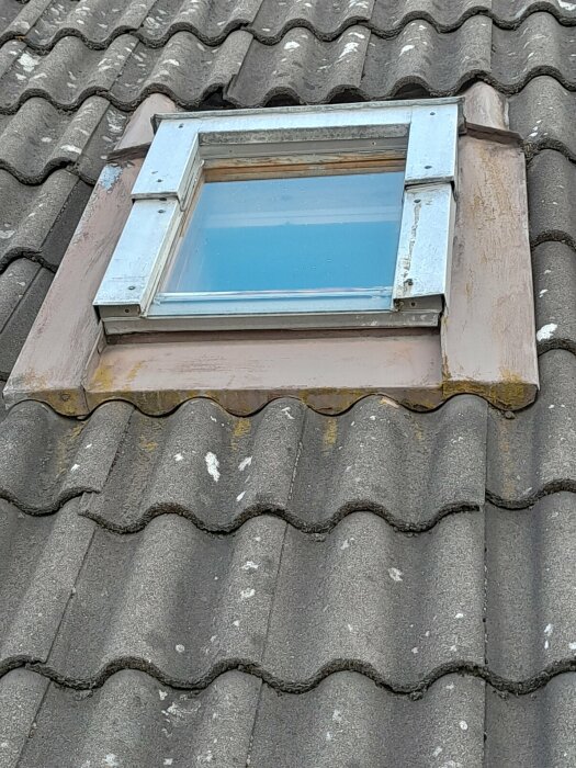Takfönster på tegelpannor, inramat av aluminium, mögel eller lavar synliga, dag med molnigt väder.