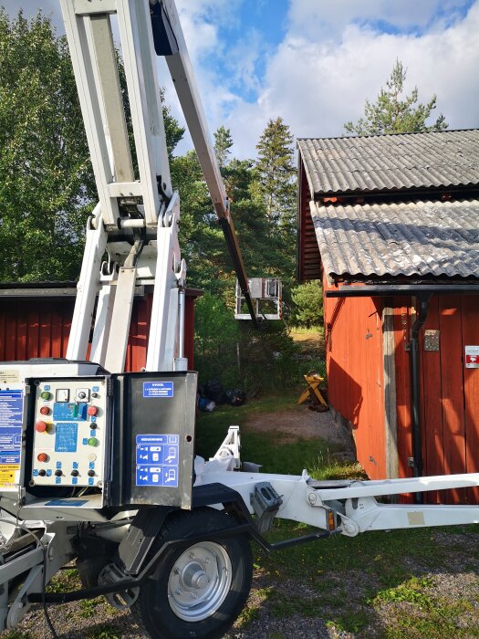 Skylift utrustning i trädgård nära röd stuga och grönska under solig himmel.