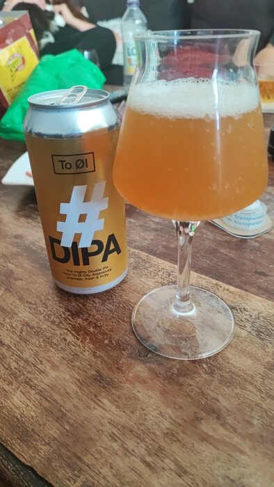 Ölburk och glas av öl på träbord; DIPA; bakgrund med suddiga personer.