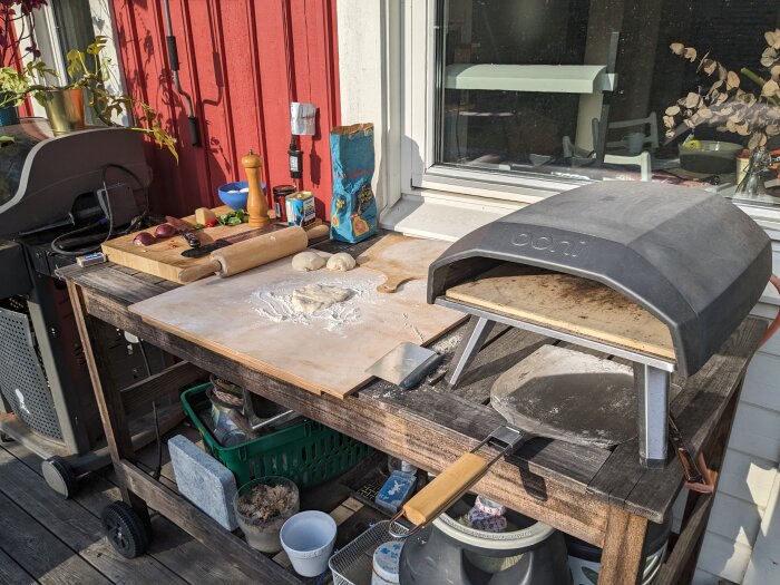 Uteplats med pizzaugn, förberedelsebänk, deg, kavel, grönsaker, matlagningsredskap och grill.