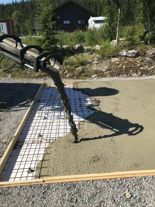 Betong hälls för fundament med armeringsnät, i soligt byggområde med skogsbakgrund.