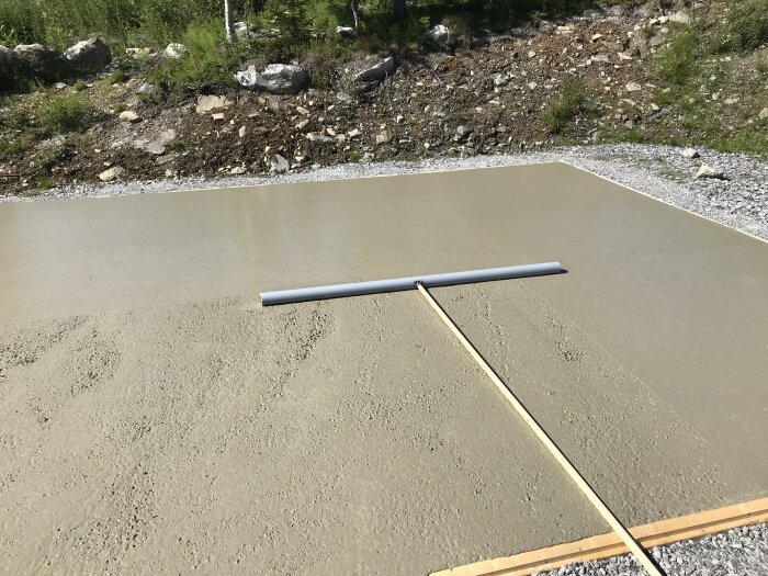 Nyutgjuten betongplatta med jämningsbräda, omgiven av grus och naturterräng.