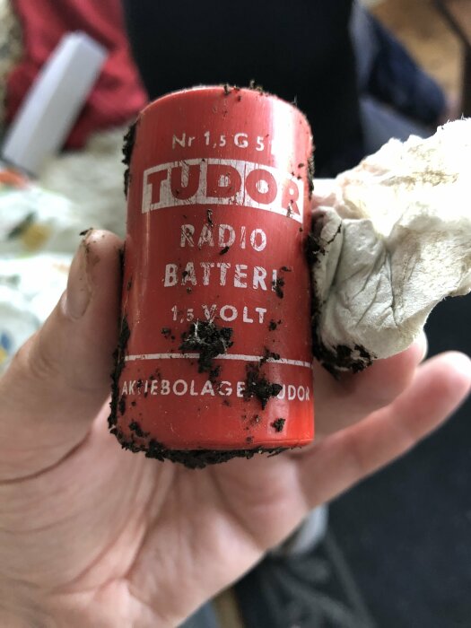 Hand håller smutsigt, gammalt Tudor radio batteri. Bakgrund oskarp, detaljer synliga.