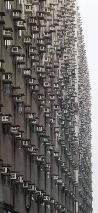 Ett höghus täckt av många likadana luftkonditioneringsenheter, tätt sammansatta balkonger, stadsarkitektur.