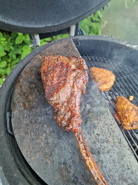 Grillad köttbit på stenplatta i rökig kolgrill, omgiven av grönska. Grillmästarens dröm.