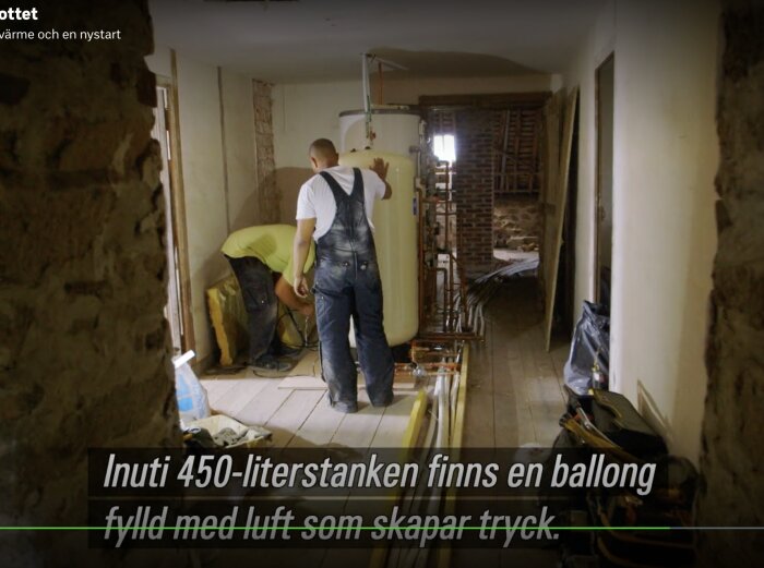 Arbetare installerar stor tank i interiör, ombyggnad pågår, verktyg syns, byggmiljö, teknisk textning på svenska.