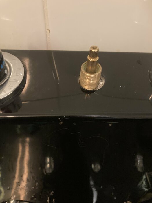 Gaskök, fjäderbelastad säkerhetsventil eller tändare, svart yta, vattenstänk, kakel i bakgrunden.