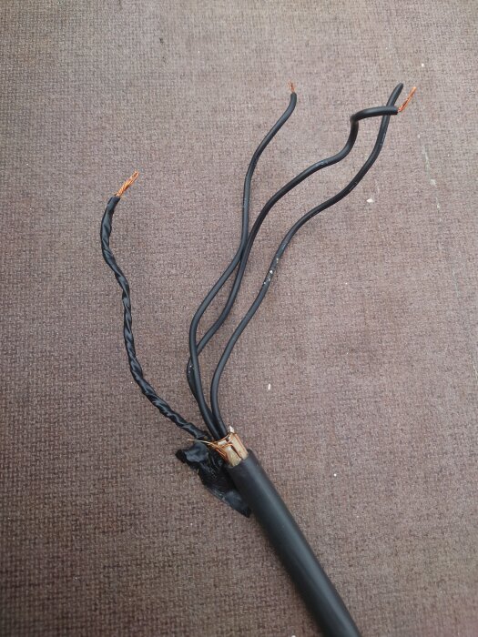 Slitet, skadat elektriskt kabel med exponerade koppartrådar på en textilbakgrund.