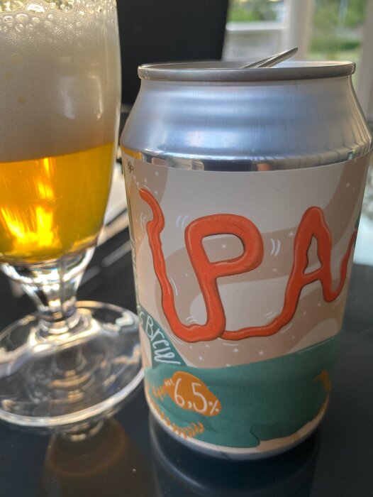 Öppnad IPA-öldrycksburk, 6,5% alkohol, nära ett fyllt glas.