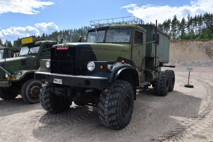 Militär lastbil, KrAZ-märke, robust, terrängduglig, grönt kamouflagemönster, utomhus i dagsljus, skog i bakgrunden.