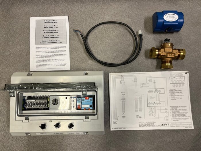 Elektrisk utrustning, ventil, kablar, instruktioner och schematiska diagram på grått underlag.