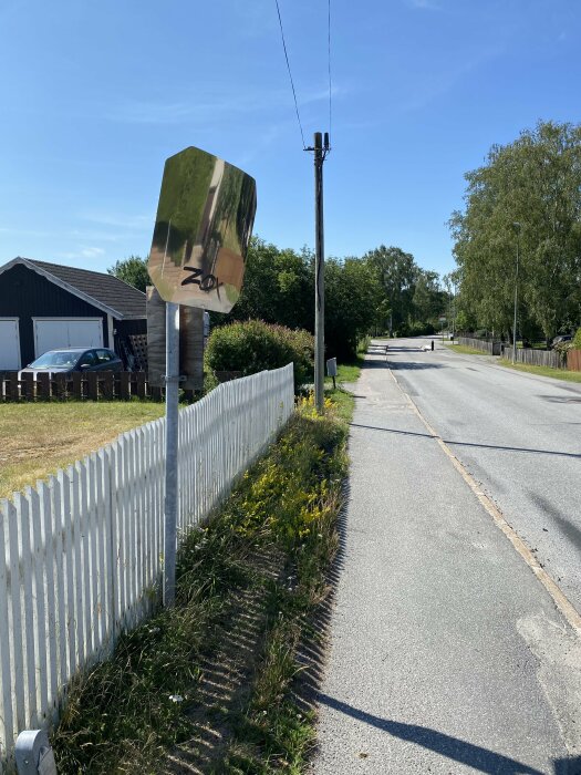 Solsken, spegelvänt stoppskylt, landsväg, vita staket, grönska, blå himmel, elstolpe, skuggor.