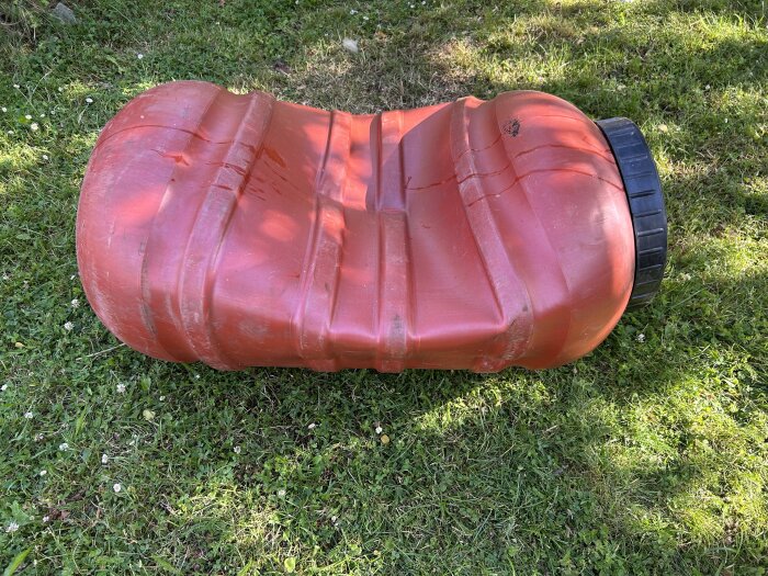 Röd uppblåsbar soffa ligger platt på gräsmatta utomhus, slitna detaljer, kopplad till avslappning eller fritid.