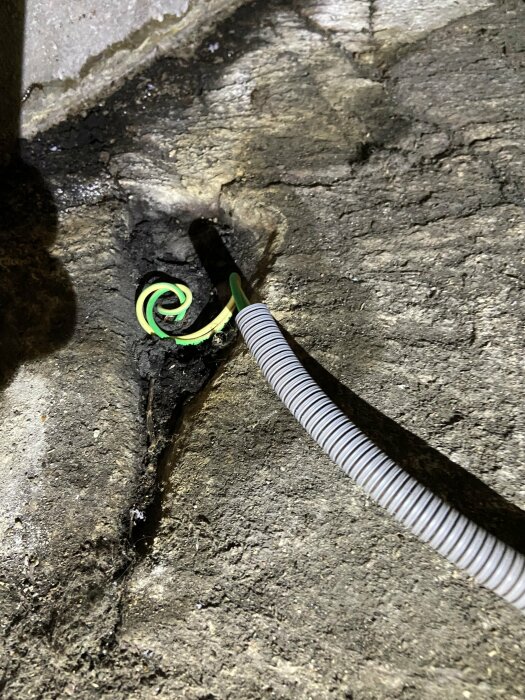En vit och svart räfflad kabel går genom ett hål i betong med en grön slinga.