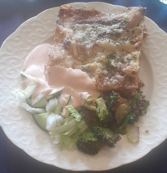 Lasagne med sallad och broccoli på en vit tallrik, matfoto, serverat måltid, troligtvis lunch eller middag.