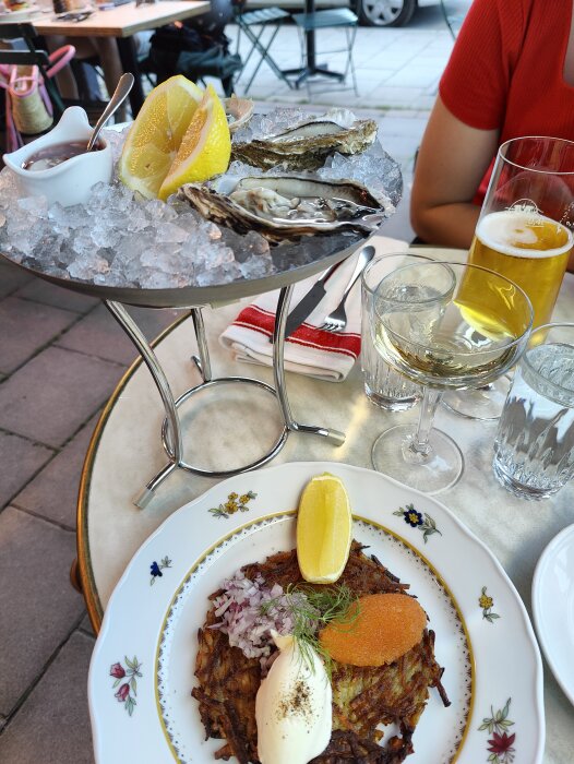 Ostron på is, citron, sås, råraka med tillbehör, öl och snaps, utomhusrestaurang, del av person i rött.