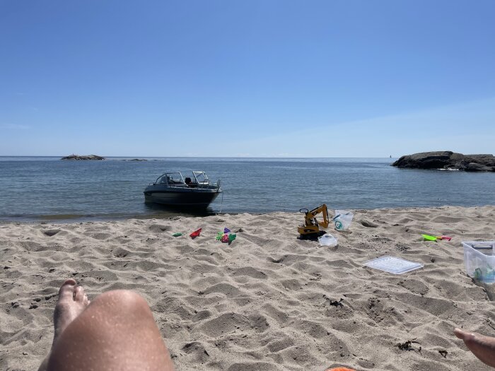 Solig stranddag, båt i vatten, leksaker i sanden, avslappnande semesterstämning.