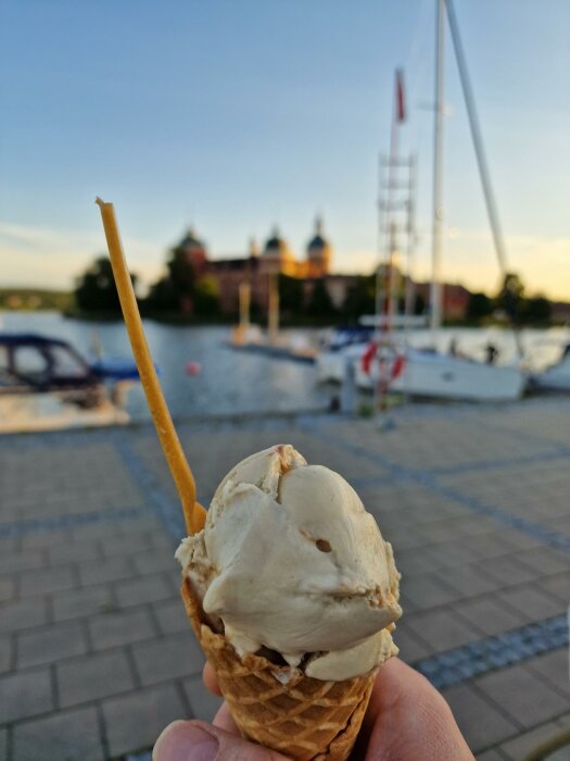 Glass i strut med segelbåtar och byggnad i bakgrunden, suddig kvällshimmel, sommarstämning vid vatten.