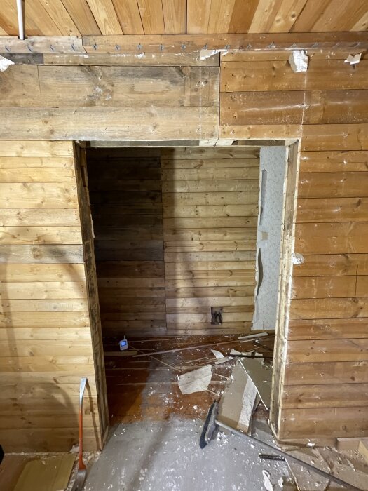 En planlagt åbning i en bærende trævæg, med synlige bjælker og rodet gulv, muligvis fra en igangværende renovering eller nedrivning.