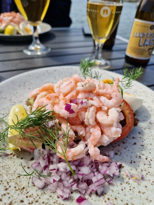 Räkmacka på tallrik, rödlök, dill, citron, två ölglas, utomhusatmosfär.