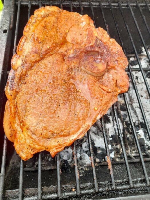 Ett stort marinerat kotlettstek grillas på en kolgrill, bubblor och saftigt, brandännmärken synliga.