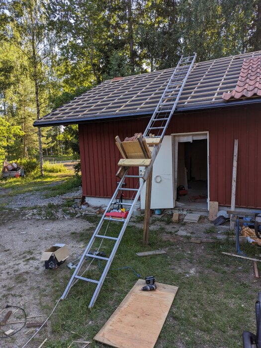 Röd stuga, solpanelinstallation, stege, verktyg, skogsbakgrund, öppen dörr, byggmaterial, dagtid.