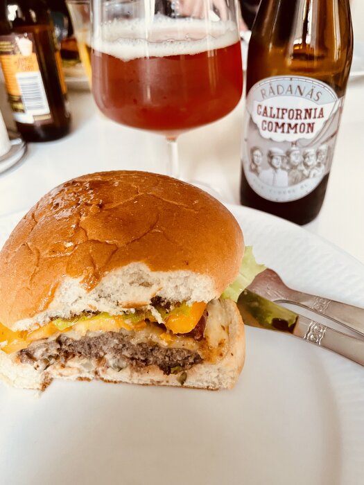 Hamburgare med bit tagen ur framför en ölglas och en flaska öl med etiketten "California Common".