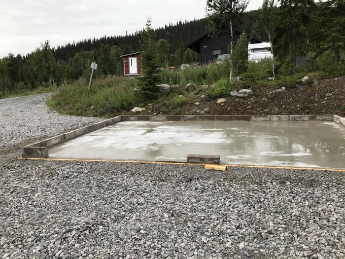 En nyligen gjuten betongplatta, troligen för en byggnadsgrund, med skogsbakgrund och grushöljd förgrund.