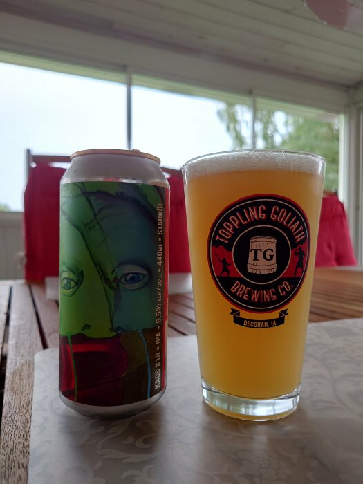 Ölburk med konstnärlig design bredvid ett glas öl, Toppling Goliath Brewing-märke, inomhus.