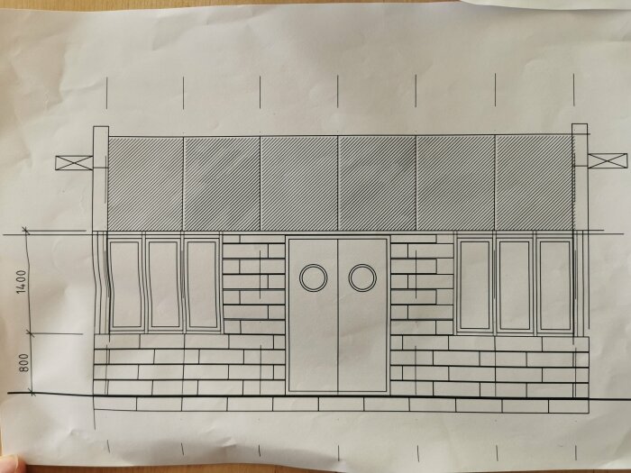 Arkitektonisk ritning av en byggnadsfasad med måttangivelser, fönster, dörrar och en sittbänk, på vitt papper.