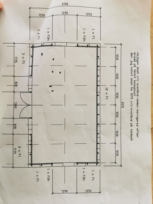 Arkitektonisk ritning, möjligtvis för en byggnad eller rum, med måttsättningar, upplagt på ett bord.