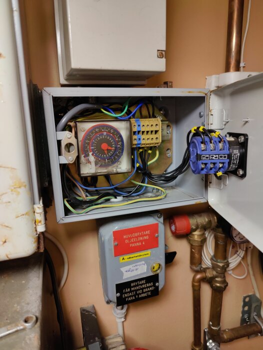 Ett öppet elektriskt skåp med regulatorer och kabeldragningar, intill rör och avstängningsventil.