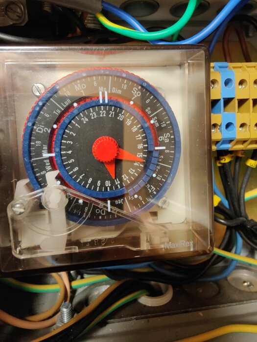 En analog timer med vecko- och dygnsskala, inställningsmarkörer, omgiven av elektriska kablar och kopplingar.