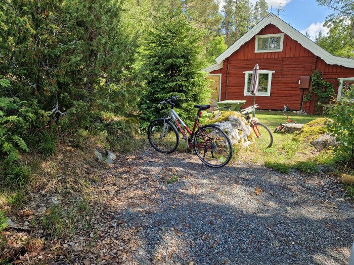 Röd stuga, grönska, cykel, soligt, grusgång, sommardag, fridfullt, svensk lantidyll.