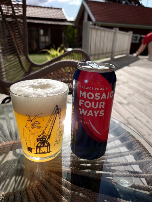 Ölglas med skum vid sidan av en burk öl på glasbord utomhus, soligt, del av trädgårdsmöbel syns.