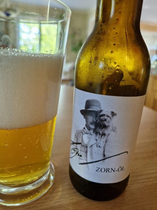 Ölflaska med etikett föreställande en man och hund, bredvid ett glas fyllt med öl.