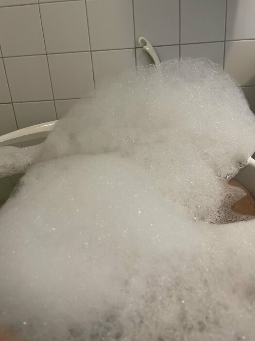 Ett överfyllt badkar med skumbad i ett kaklat badrum.