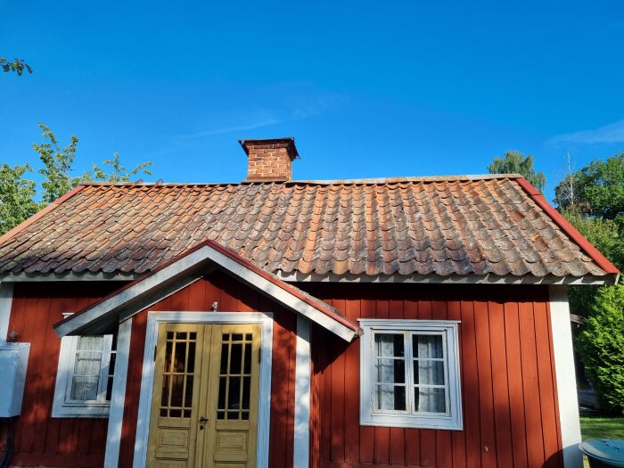Rött trähus med tegeltak, skorsten och soligt väder.