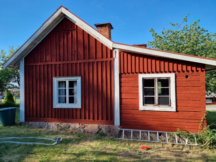 Rött trähus med vita fönsterkarmar, tegelskorsten, grund av natursten och soligt grönt gräs.