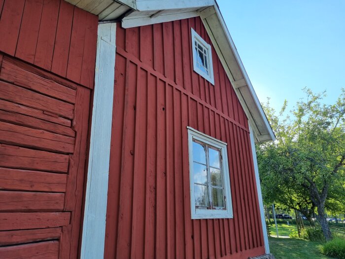 Röd trästuga, vita fönsterkarmar, gröna träd, blå himmel, traditionell svensk arkitektur, utomhus, dagtid.