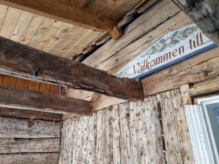 Träväggar och bjälkar med skylt "Välkommen till" och dekorativa blommor. Rustik, traditionell stil.