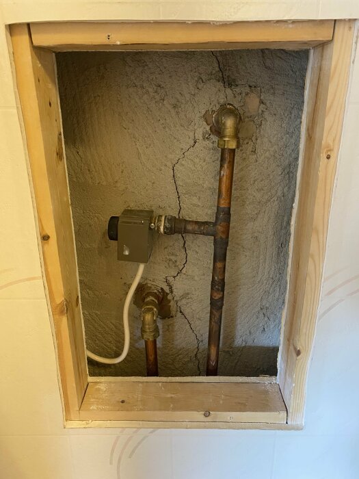 Vattenledningar och en mätare i en öppen inspektionslucka med spruckna väggar inuti.