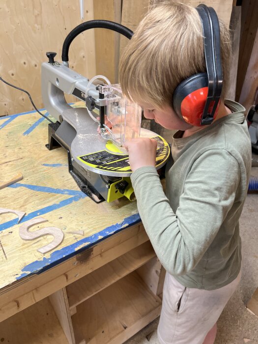 Pojke använder dekupersåg med hörselskydd i verkstad.