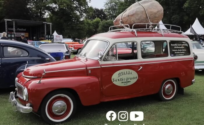 Röd och vit veteranbil med stor sten på taket, uppställd vid bilfestival.