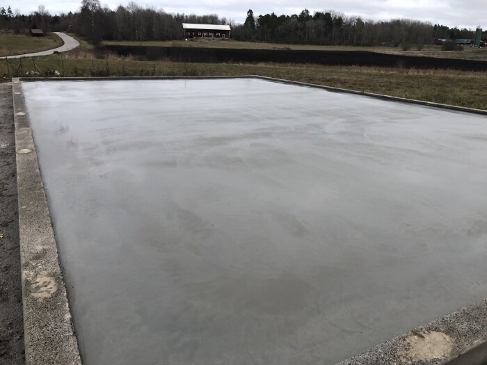 Nyjuten betongplatta, molnig himmel, landsbygdsväg, träd, hus i bakgrunden, lugn landsbygdsscen.