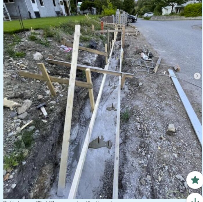 Byggarbetsplats med trähjälpmedel uppställda för trottoarkant, ojämn mark och byggmaterial synligt.