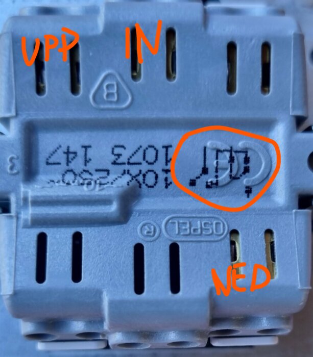 Elektronisk komponent med märkning, cirklanderat ID, och ordet "UPP" uppåt, "IN" pekande inåt, "NED" nedåt.