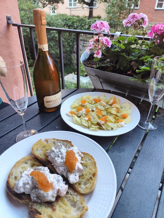 Uteplats med mat: skaldjursmackor, chips, cava och blommande pelargon. Avkopplande atmosfär med balkong utsikt.