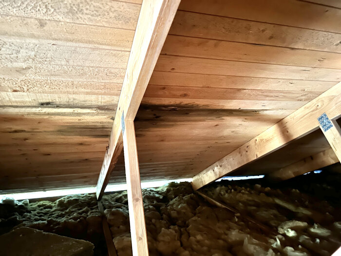 Bild av vindsutrymme med träbjälkar, isolering, och synligt undertak.